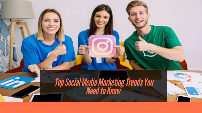 Three young adults smiling and sitting at a table with laptops and social media logos like LinkedIn and Instagram, holding an Instagram logo cutout. Text overlay reads, "Top Social Media Marketing Trends You Need to Know."